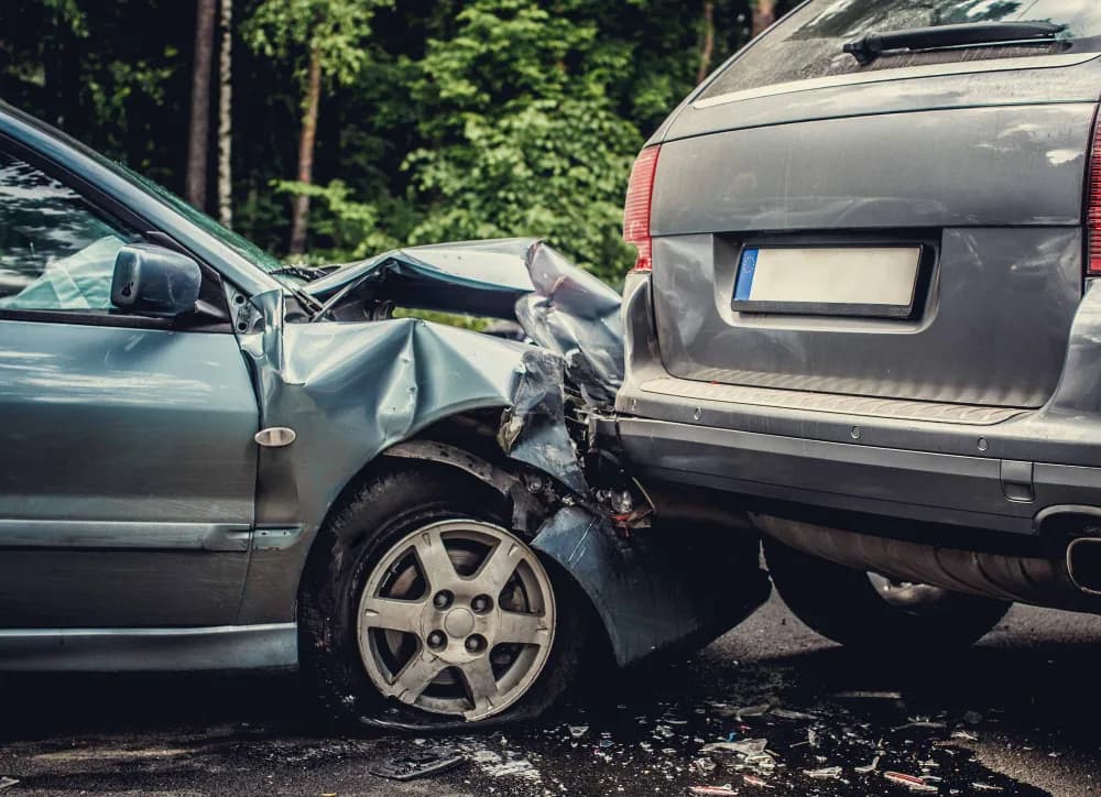 Close-up of two cars after a rear-end collision with a crushed front fender and debris on the road