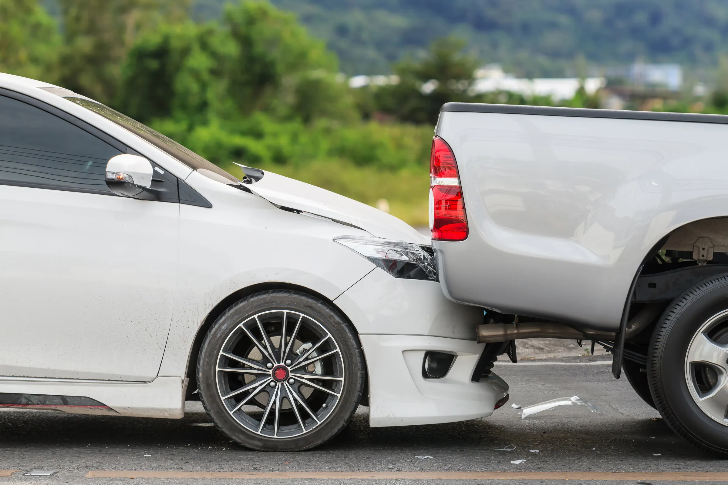 White sedan that rear-ended a silver pickup truck, with a dented hood and broken headlight